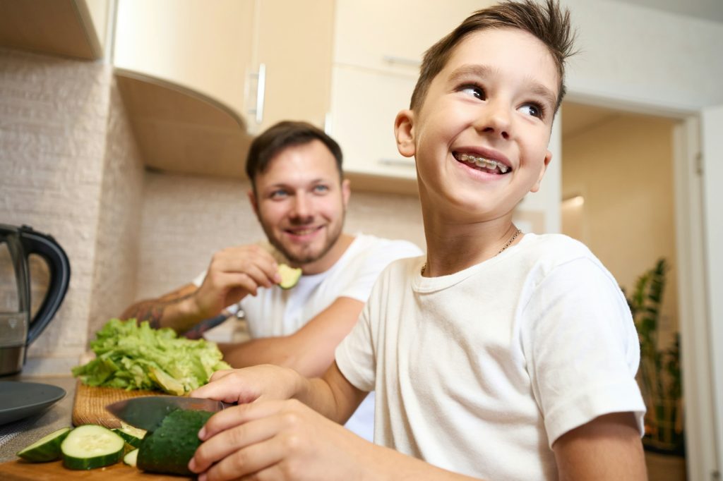 Boy with teeth braces smiling while cutting cucumber