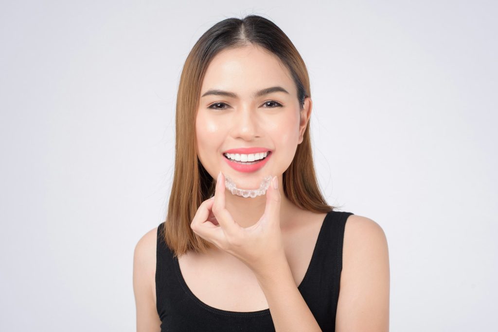 Young smiling woman holding invisalign braces in studio, dental healthcare and Orthodontic concept.